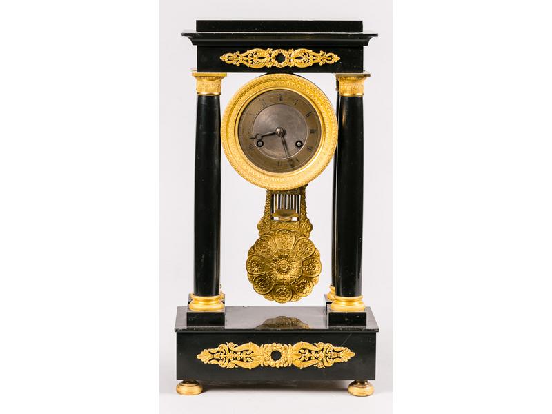 Pendule portique flanquée de quatre colonnes, en marbre et placage de marbre noir.  Le cadran en fer.  Ornementation en bronze.  Epoque Restauration.  Hauteur : 41.5 cm. (petites restaurations)
