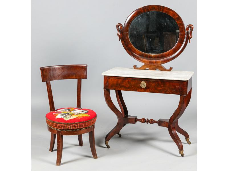 Coiffeuse d'époque Restauration en placage d'acajou ouvrant en ceinture par un tiroir découvrant une petite table gainée de cuir et reposant sur quatre pieds en console à roulette. Plateau de marbre blanc surmonté d'un miroir de forme ovale pivotant à col de cygne. On y joint une petite chaises en a