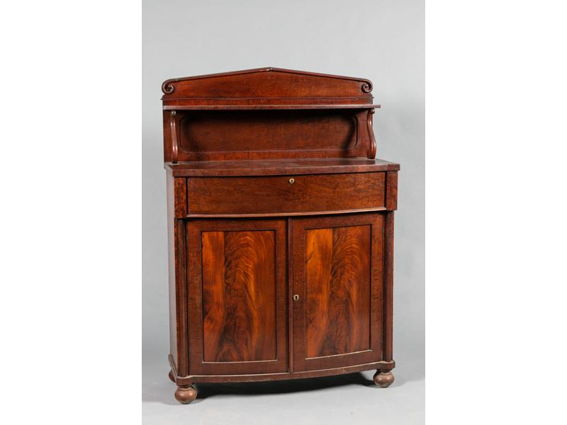 Buffet-desserte en placage d'acajou à façade ceintrée ouvrant par un tiroir et deux portes.  Le plateau surmonté d'une étagère en gradin reposant sur des petites consoles.  Epoque fin XIXe siècle.  Dim.: 147x101x44 cm.
