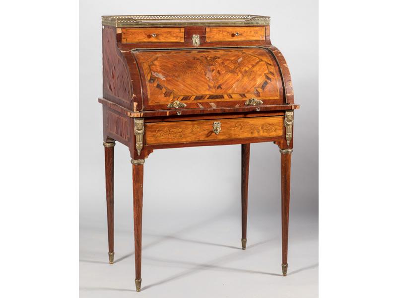Secrétaire cylindre de style Louis XVI, en bois marqueté (nombreux sauts de placage et manques à la marqueterie). Il ouvre par un tiroir en ceinture, deux autres en gradin et par un cylindre dégageant un pupitre gainé de cuir. Epoque XIXème siècle. Dimensions : 117x75x54 cm