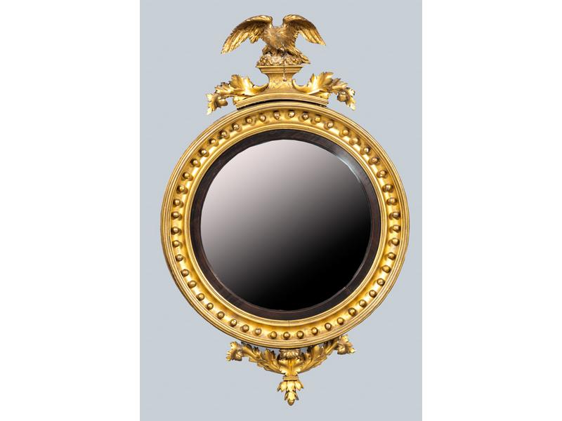 Joli miroir circulaire et bombé dans un encadrement en bois sculpté et doré à décor de perles, feuillages.  Il est surmonté d'un aigle aux ailes déployées.  Angleterre.  XIXe siècle.  Hauteur : 102 cm.  Diamètre : 64 cm. (infimes accidents et redorures)