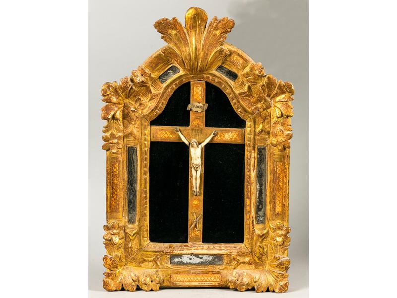 Christ en ivoire dans un encadrement à fronton à parecloses en bois doré orné de fleurs et feuillages.  XVIIIe siècle.  Dim.: 55x36 cm.