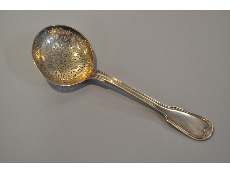 Cuillère saupoudreuse en argent (poinçon Minerve) à décor ajouré rayonnant et filets.  Spatule à décor d'un écusson chiffré.  Poids : 109g.