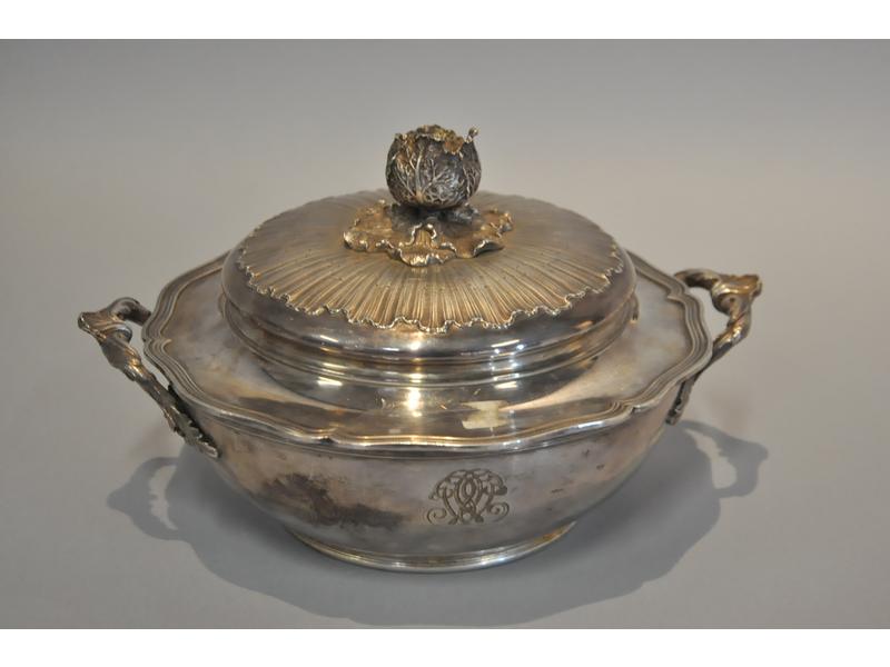 Légumier en argent de style Louis XV à anses à décor feuillagé.  Couvercle à décor chiffré, fretel en forme de chou ciselé sur un fond rayonnant.  Poinçon Minerve.  Maître orfèvre : Boin Taburet à Paris.  Poids : 1014g.