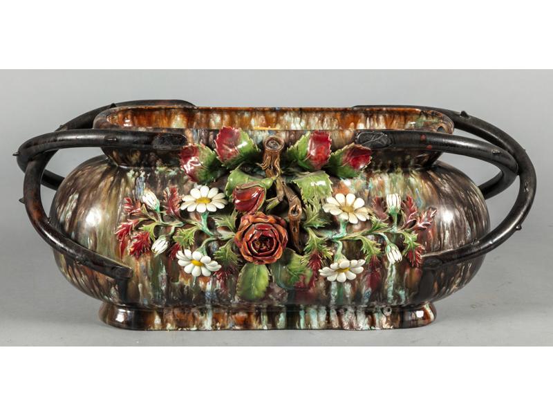 APT - La Croix : Jaridinère de forme oblongue en faïence jaspée et barbotine.  Panse ornée (sur un seul côté) d'un grand bouquet de fleurs en relief.  les anses à l'imitation de branches d'épineux.  Porte l'étiquette de la manufacture.  Hauteur : 25 cm.  Longueur : 61 cm.
