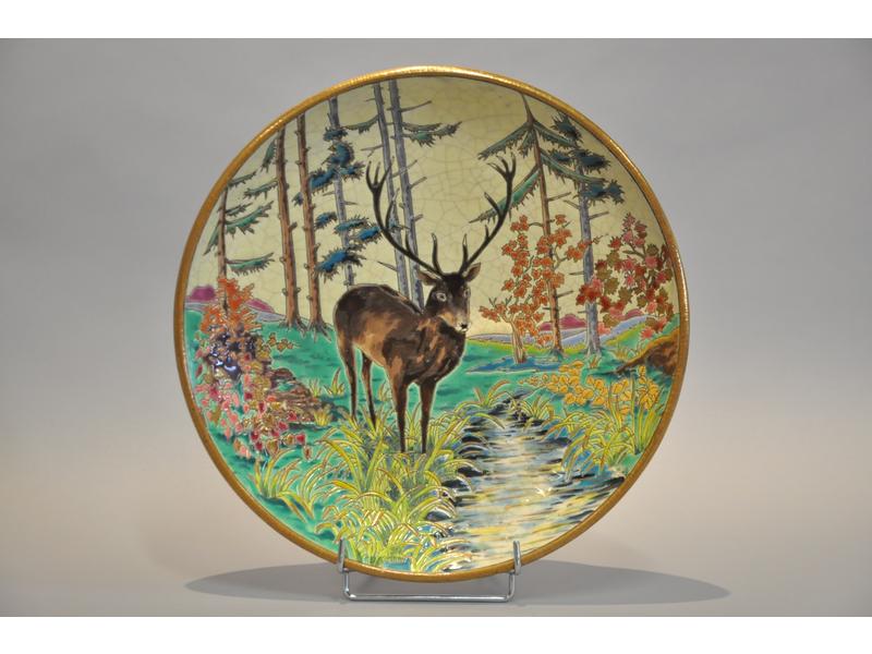 LONGWY : Grand plat en faïence à décor émaillé d'un cerf près d'une pièce d'eau.  Marqué.  Diam.: 38 cm.  Bon état.