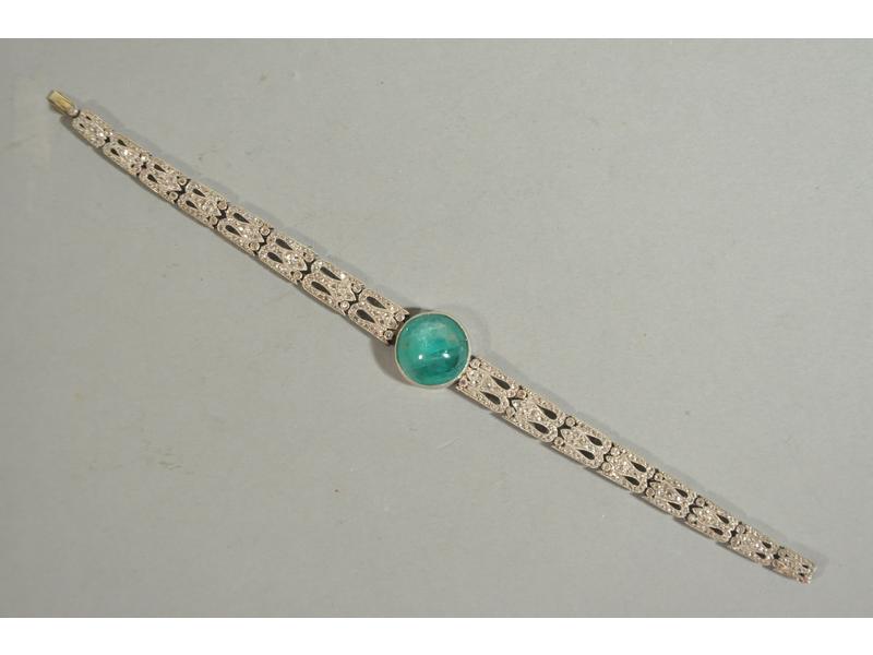 Bracelet articulé en or gris composé d'une chute de maillons ajourés en fleurons sertis clos de diamants taillés en rose, et orné en son centre d'une émeraude taillée en cabochon rond (15.2x7.8 mm environ).  Années 1910.  Long.: 181 mm.  Poids brut : 23g50.
