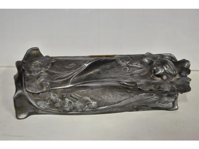 Joli coffret à bijoux d'époque Art Nouveau en étain à décor en relief d'un buste de femme et fleurs.  Il ouvre sur un intérieur capitonné.  Long.: 34 cm.