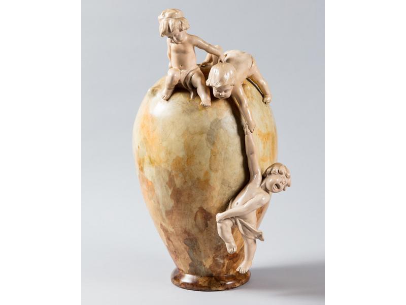 GOLDSCHEIDER - Autriche : Vase en terre cuite à émail marmoréen orné en haut-relief de trois enfants s'amusant autour du vase en haut-relief.  Signé.  Hauteur : 52.5 cm. (petits accidents et reprises à l'émail)