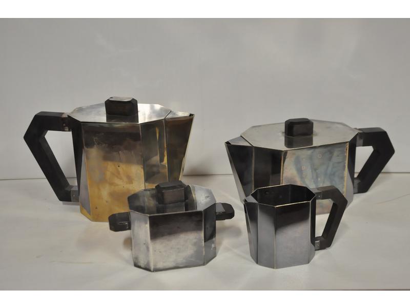 Service à thé et café en métal argenté.  Panses à pans coupés.  Fretes et poignées en bois noirci.  Epoque 1930.  Hauteur cafetière : 15.5 cm. (parties légèrement désargentées, soudures)