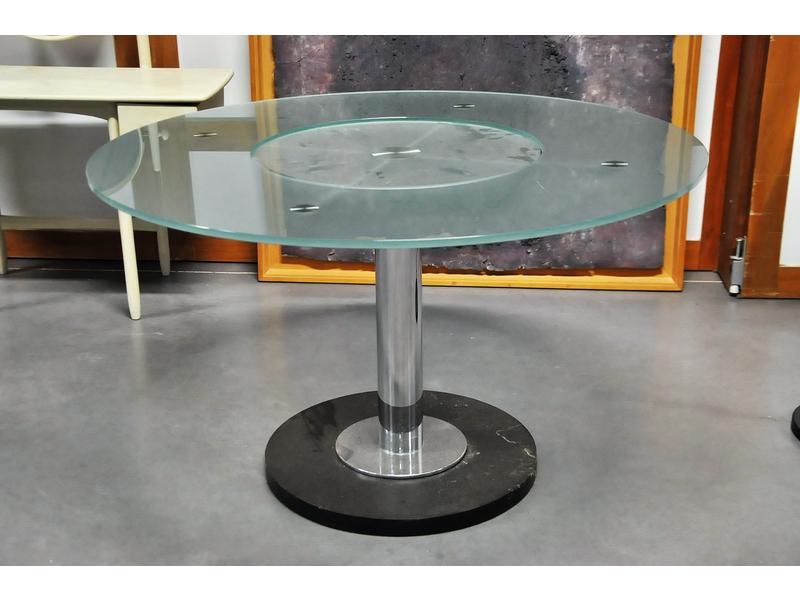 Table ronde, plateau à dalle de verre dépolie et découpée, avec centre tournant, reposant sur une monture et un fût en métal chromé.  Base circulaire en bois laqué noir.  Diam.: 125 cm.  Hauteur : 74 cm.