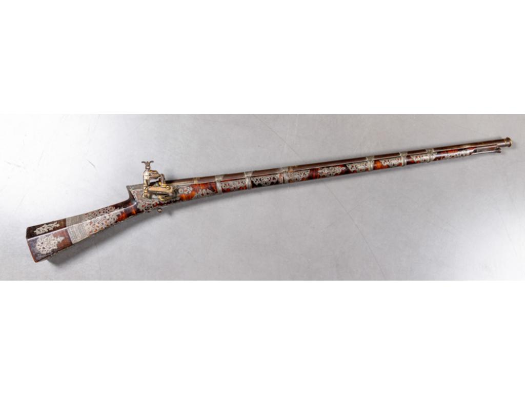 Beau fusil à silex ottoman Tüfek. Canon rond, à bourrelet à la bouche, patiné tabac, décoré à l r de rinceaux feuillagés. Platine à la Morlaque décorée en suite à l r. Détente en bouton, à pans. Bagues de canon en argent. Monture et crosse à pans en noyer flammé richement décoré d ncrustations d rgent découpé et gravé à décor de rinceaux (manque une bague à l vant du fût). Baguette en fer.