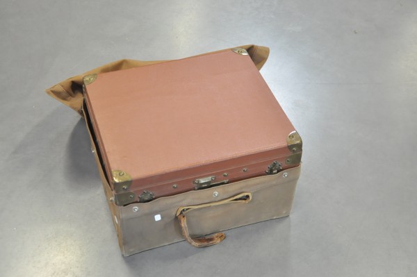 Petite malle de voyage recouverte d'une toile, avec étiquettes de transport des années 30.  Dim.: 42x25x36 cm. (poignée cassée)