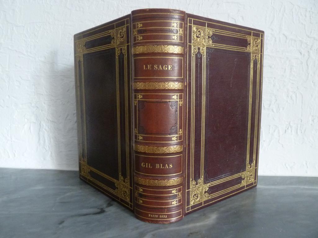 LE SAGE : Histoire de Gil Blas de Santillane. Paris : Paulin, 1835. Un volume grand in-8°. Reliure de lépoque plein maroquin lie de vin, dos à 4 nerfs sautés élégamment orné de dencadrement de filets dorés et à roulettes à froid, plats richement ornés de jeux de filets dorés et à froid formant encadrement avec aux écoinçons de beaux fleurons dorés sur un semé de points, double filet doré sur coupes, double filet doré avec fleuron doré aux angles sur chasse, tête rouge. Non rogné. Illustré en 1er tirage du portrait de Gil Blas, gravé sur bois et tiré sur Chine, 600 gravures sur bois in-texte de Jean GIGOUX. Double encadré en noir du texte. (Carteret : . Brivois : 256. Carteret : III, 382). Des rousseurs parfois fortes en tête principalement, deux feuillets parfaitement et discrètement restaurés en marge, dos un brin plus clair, BON EXEMPLAIRE de cette édition de Gil Blas qui marque la rénovation de la gravure sur bois à lépoque romantique. La reliure bien que non signée, sort indiscutable de latelier dun grand relieur