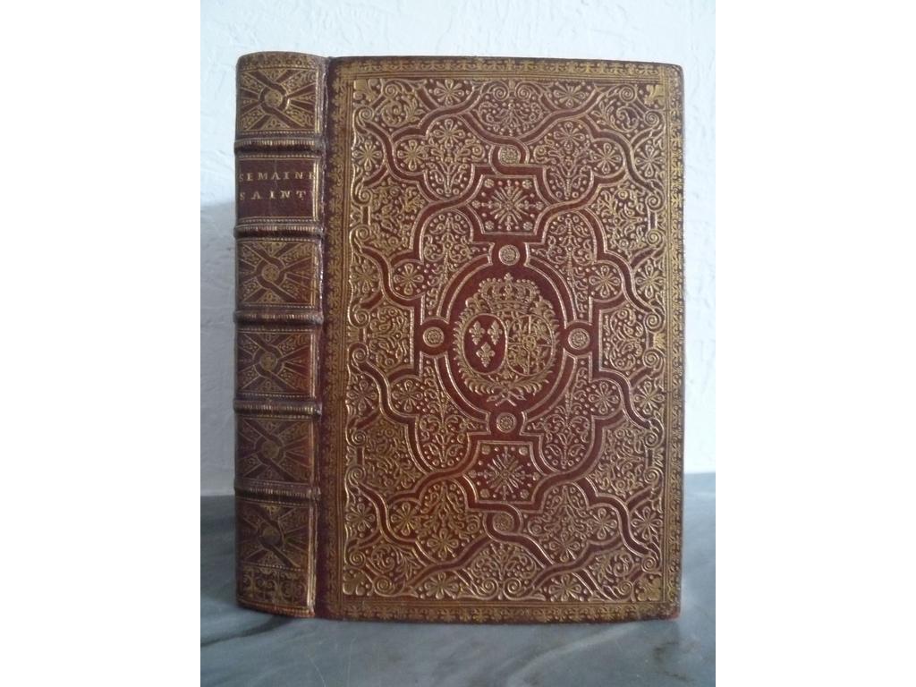 Office de la semaine sainte en latin et en français à lusage de Rome et de Paris  Paris : Veuve Mazières er Garnier, 1728. Un volume in-8°. Reliure de lépoque plein maroquin rouge, dos à nerfs orné de caissons de double filet doré fleuronnés et fleurdelysés au centre, plats richement orné de riches compartiments dorés à la fanfare composés dentrelacs de quadruples filets dorés ornés de feuillages, rinceaux et fleurons frappés au pointillé, petite dentelle dorée en encadrement, armes dorées au centre de la reine Marie LECZINSKA, dédicataire de lédition, roulettes dorées sur coupes et chasses, toutes tranches dorées, doublure et gardes de papier doré orné d'un décor floral peint au pochoir. Page de titre gravée, vignette de dédicace aux armes de la Reine et 3 gravures hors-texte par SCOTIN. Des feuillets brunis, ex-dono sur verso garde, cachet humide répété sinon TRES BEL EXEMPLAIRE, fort bien conservé en maroquin rouge orné à la fanfare et aux armes.